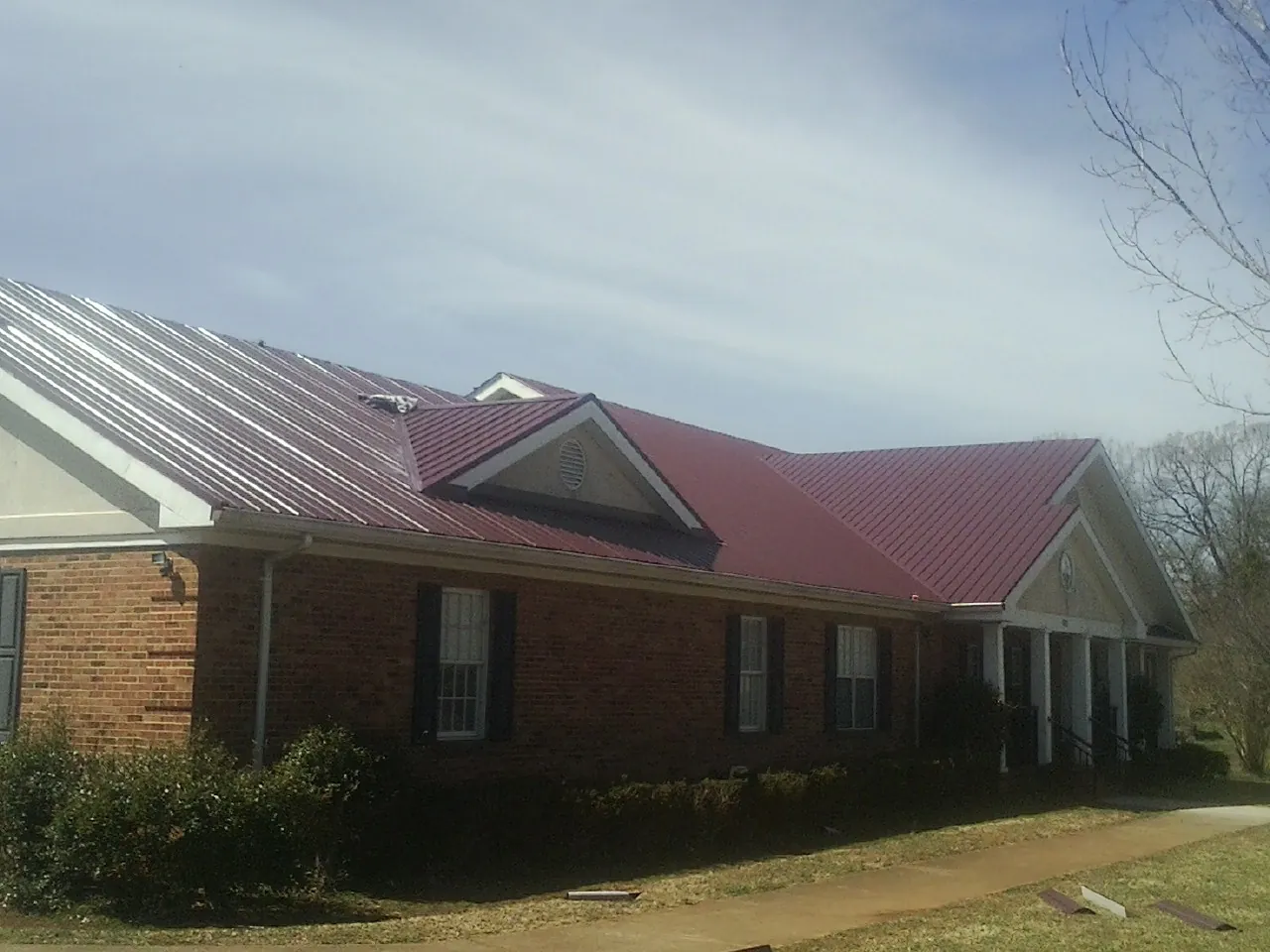 Red metal roof with gabled entries on a long brick building, from a Hail Damage Roof Repair job in Danvers